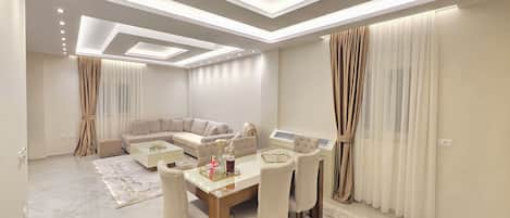 A modern living room with a sectional sofa, a dining table with chairs, and a ceiling with recessed lighting.