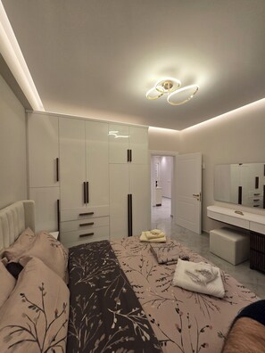 A modern bedroom with a bed, a wardrobe, a vanity with a mirror, and a hallway leading to another room.
