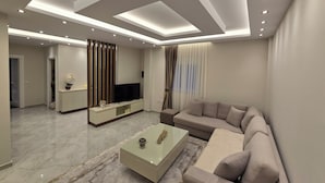Ein modernes Wohnzimmer mit Fernseher, Sofa, Couchtisch und einem gemusterten Teppich.