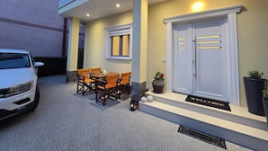 Ein Gebäude mit Balkon, Tisch mit Stühlen, ein Auto und eine Tür mit Fußmatte.