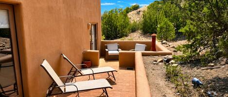 A patio with lounge chairs and a small table, a door, and a view of a natural landscape with trees and hills.