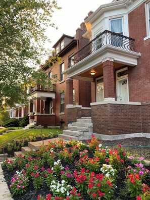 A residential building with a brick facade, a front porch, and a small garden with colorful flowers. - Serene 2-bedroom apartment with concierge in vibrant St. Louis (St. Louis)