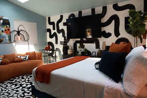 A modern bedroom with a bed, a sofa, a desk, and a large abstract wall art. - The Skylight Studio- A Hidden Gem (Atlanta)