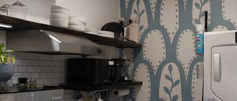 Una cocina con estufa, horno, microondas y refrigerador. Hay repisas sobre la estufa con platos y un jarrón azul.