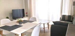 A modern living room with a flat-screen TV, a dining table, and a sofa. - Helios House - New Build - 2bedrooms & Parking (Metamorfosi)