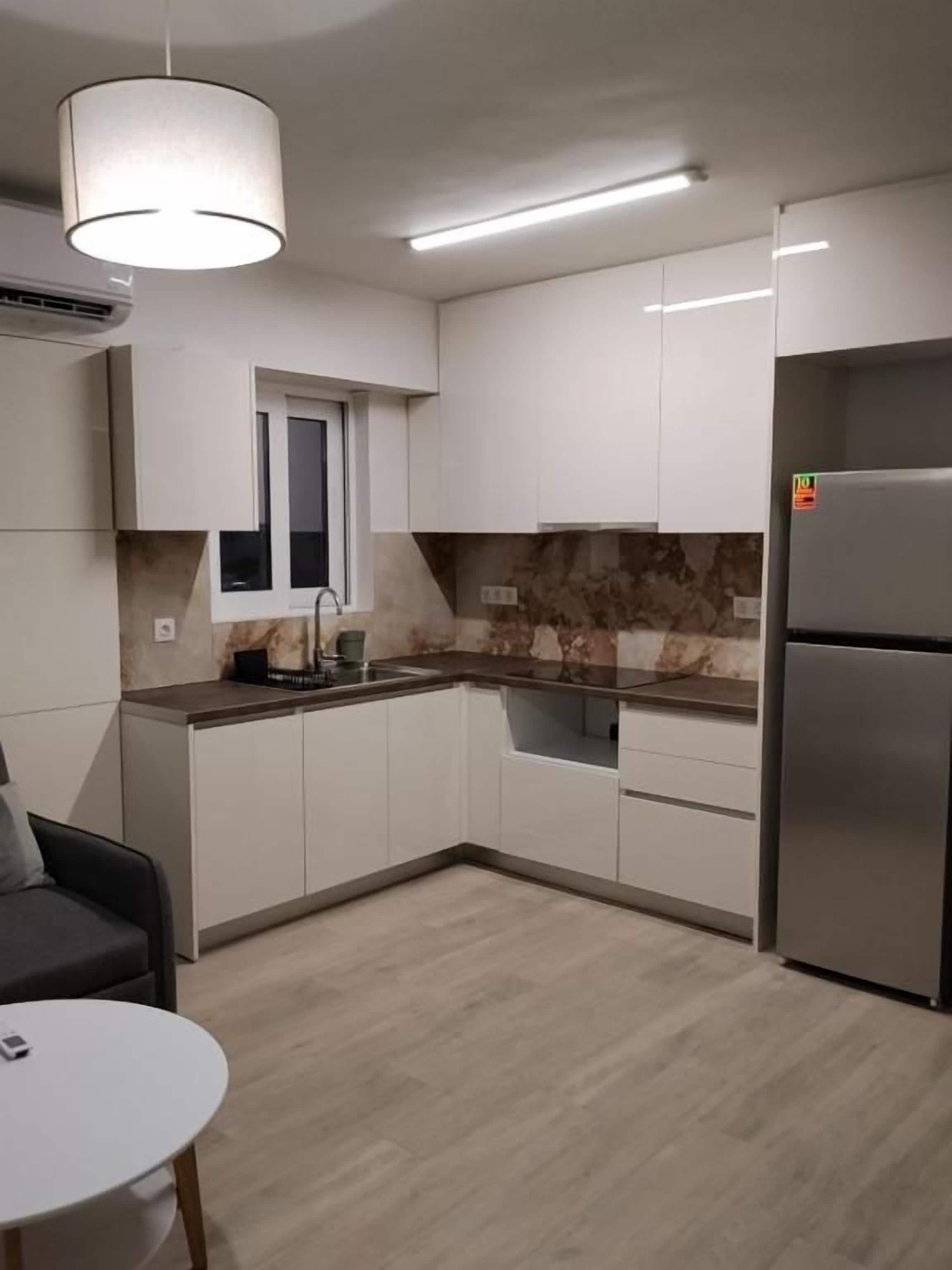 Cozinha moderna com armários brancos, forno embutido e geladeira de aço inoxidável.