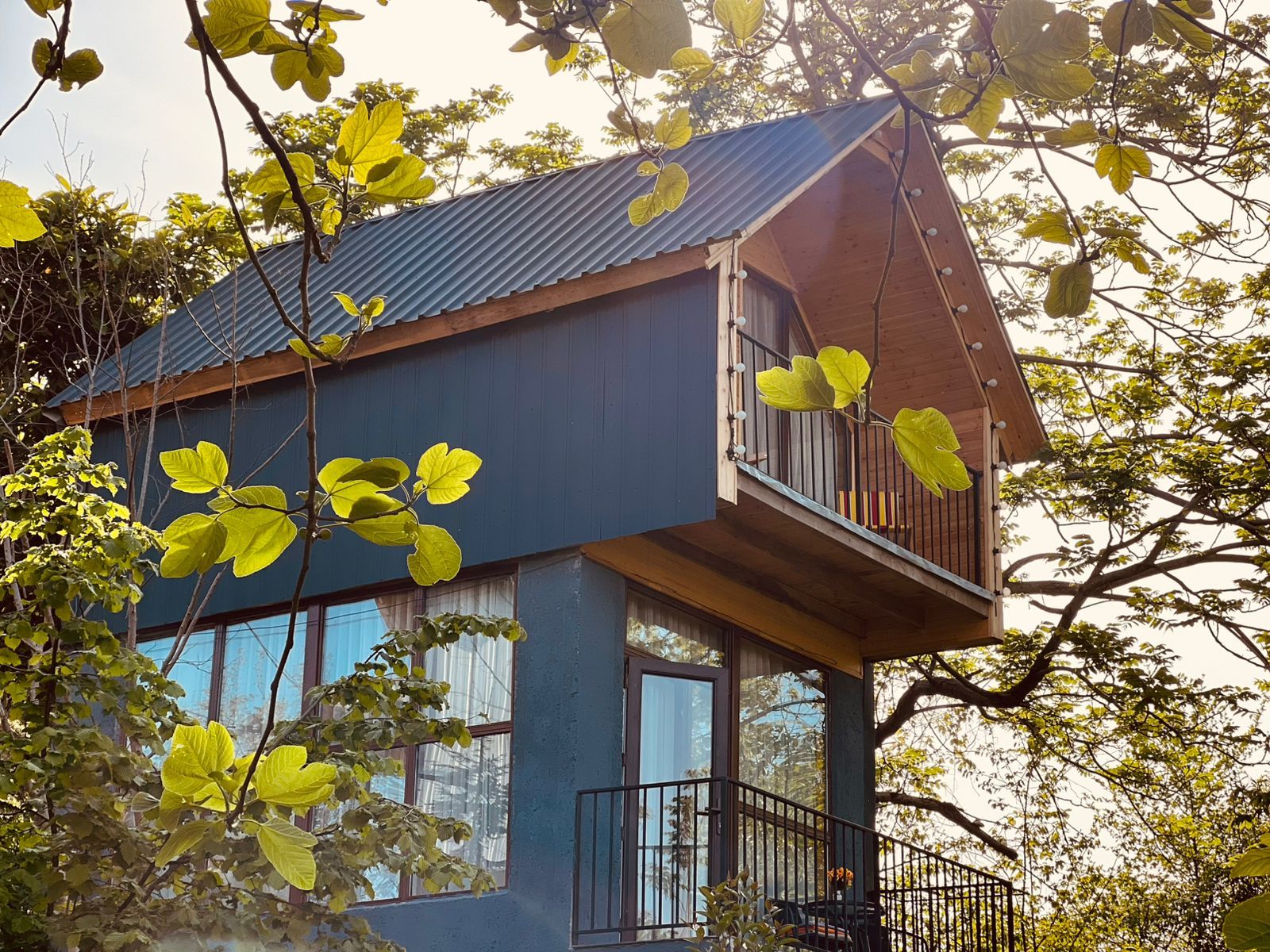 A two-story house with a balcony, large windows, and surrounded by trees.