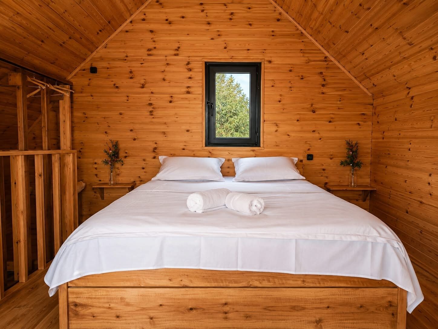 A wooden cabin bedroom with a single bed, a window, and a small table with a plant.
