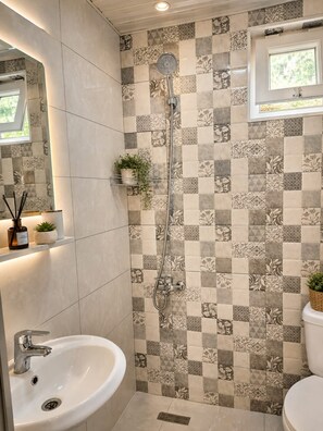 A bathroom with a checkered tile wall, a shower, a sink, and a toilet. - Cottage Buknari (Diviti)