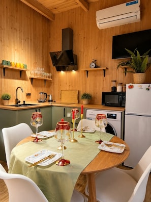 A compact kitchen with wooden walls, a dining table set for four, and a microwave. - Cottage Buknari (Diviti)