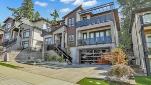 A modern multi-story residential building with a garage entrance, outdoor stairs, and a landscaped area with a small tree and decorative pots. - Manzil Suite | Cozy 2BR Private Retreat (Maple Ridge)
