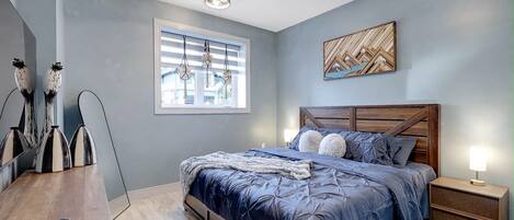A bedroom with a bed, bedside tables, a window with blinds, and wall art.