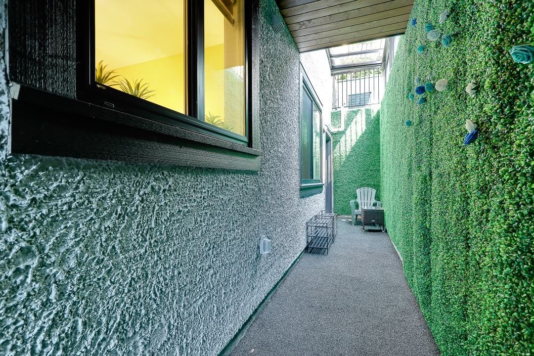 A narrow pathway flanked by a textured wall and a hedge with decorative elements.