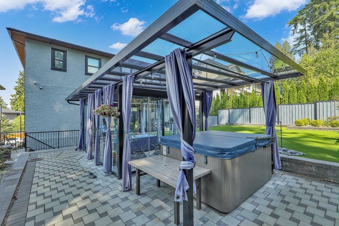 Un espace patio comprenant un jacuzzi, une table en bois et une véranda fermée par des rideaux.