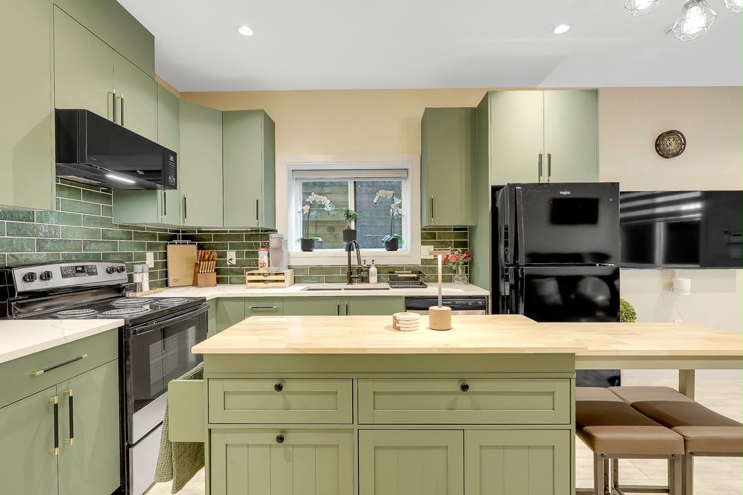 A modern kitchen with green cabinets, a central island, and a black refrigerator.