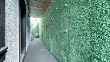 A corridor with a green hedge wall, a concrete floor, and a wooden ceiling.