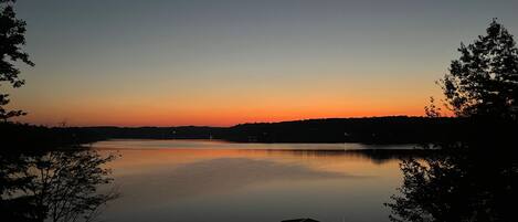 Un lago tranquilo al atardecer con un muelle y un edificio pequeño, rodeado de árboles.