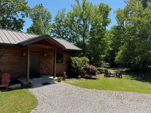 Une cabane en bois avec une allée en gravier, un porche couvert et une terrasse aménagée avec du mobilier d’extérieur.