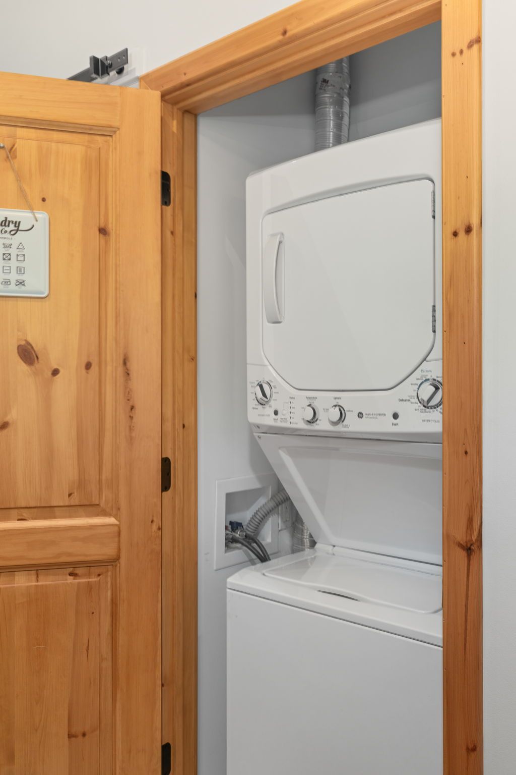 Une buanderie avec un lave-linge et un sèche-linge blancs, des armoires en bois et un panneau indiquant les services de blanchisserie.