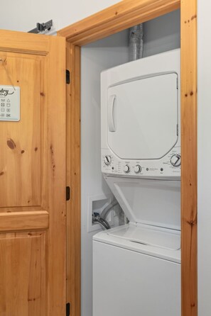 Ein Waschraum mit einer weißen Waschmaschine und einem Trockner, Holzschränken und einem Schild, das Wäscheservice anbietet.