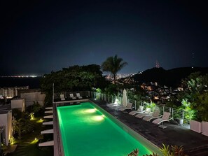 A rooftop pool with lounge chairs and a view of a cityscape at night. - Casa Zoe (Puerto Vallarta)