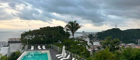 A rooftop pool with lounge chairs and a view of the city and sea.