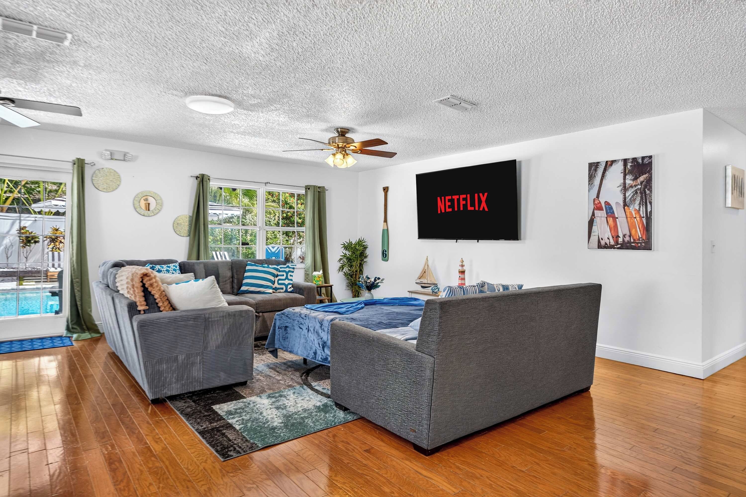 Un salon moderne doté d’un téléviseur à écran plat, d’un ventilateur de plafond et d’une grande fenêtre avec des rideaux.
