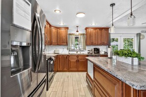 A modern kitchen with wooden cabinets, stainless steel appliances, and a marble countertop. - Heated Pool + Game Room, Near Clearwater Beach (Largo)