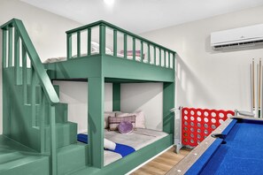 A bunk bed with a green railing, a small seating area with cushions, and a red playpen. - Heated Pool + Game Room, Near Clearwater Beach (Largo)