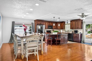 A spacious kitchen with wooden cabinets, a central island, and a dining area with a wooden table and chairs. - Heated Pool + Game Room, Near Clearwater Beach (Largo)
