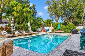 A swimming pool with lounge chairs and umbrellas, surrounded by tropical vegetation. - Heated Pool + Game Room, Near Clearwater Beach (Largo)