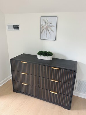 A dark wooden cabinet with vertical lines and gold handles, a small green plant on top, and a palm tree artwork on the wall. - NEW LISTING! Escape to the Cape Beach Retreat (Cape May)