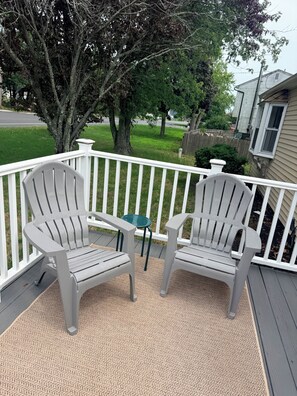 Une terrasse avec deux fauteuils Adirondack et une petite table, le tout entouré d’une balustrade blanche.