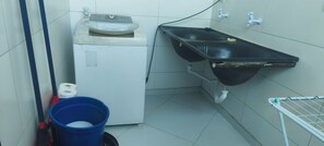 Casa de banho compacta com máquina de lavar, pia e um balde azul.
