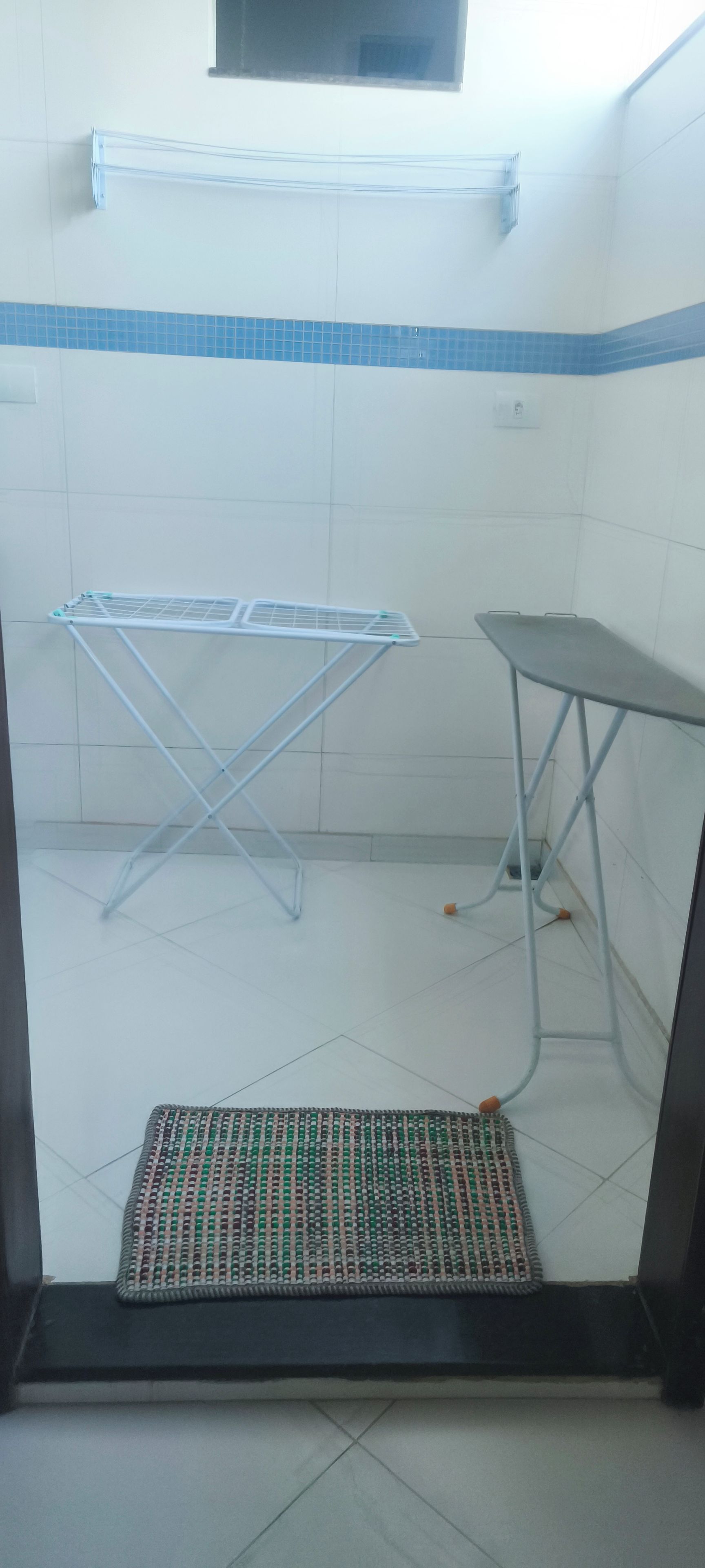 Una habitación con un tendedero, una mesa plegable y un tapete estampado en el suelo.