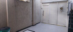 Un callejón estrecho con una puerta blanca cerrada, un contenedor de basura y una pared con textura.