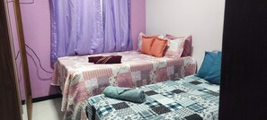 Quarto com duas camas, cortinas roxas e colcha florida.