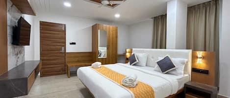 A hotel room with a bed, a bedside table, a mirror, a ceiling fan, and a wall-mounted TV.