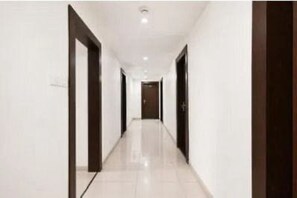 Un pasillo con paredes blancas y puertas de madera oscura, que lleva a una habitación con una puerta al final.