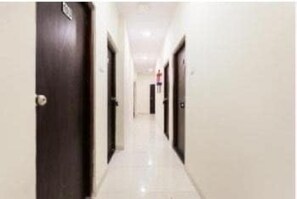 A corridor with doors on both sides, leading to a room with a visible window. - Deluxe Room the Cozy Stay (Indore)