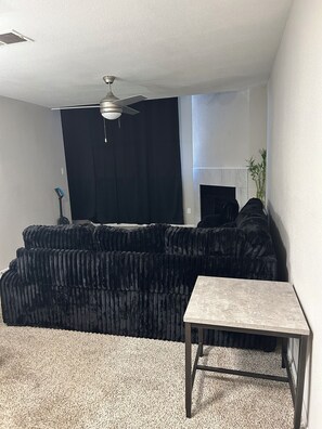 A living room with a black sectional sofa, a small table, a ceiling fan, and a window with a dark curtain. - Cozy 1-bedroom apartment in brilliant Houston with AC (Houston)