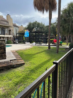 A well-maintained grassy area with a pool, a black metal fence, and a building with a balcony in the background. - Cozy 1-bedroom apartment in brilliant Houston with AC (Houston)