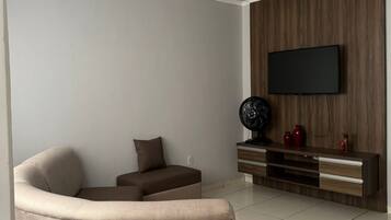 Een moderne woonkamer met een flatscreen televisie aan een houten wand, een beige bank en een klein tafeltje met decoratieve objecten.
