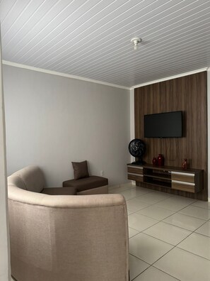 Un saló modern amb televisió de pantalla plana penjada a una paret de fusta, un sofà beix i una taula petita amb objectes decoratius.