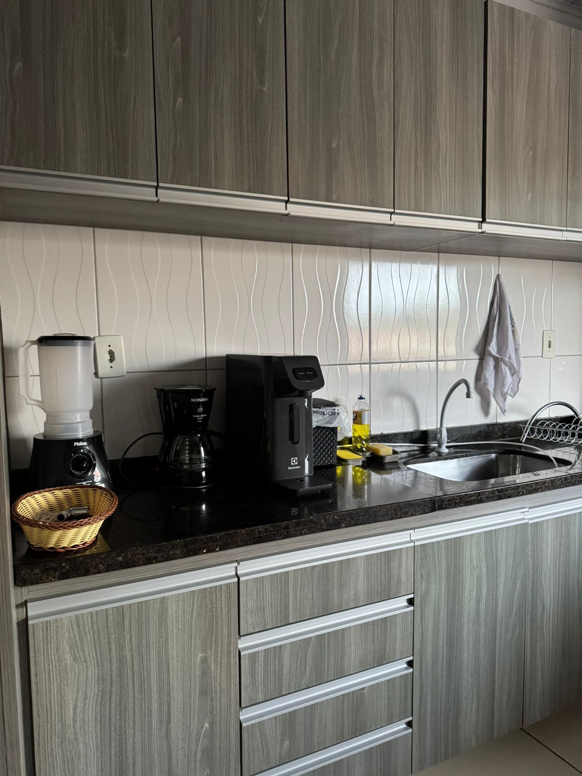 Eine Küche mit schwarzer Arbeitsplatte, einer Kaffeemaschine, einem Mixer und einem Spülbecken.