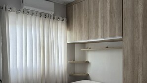 Une chambre à coucher avec un lit, une petite table, une armoire et une fenêtre avec des rideaux.