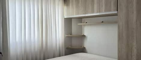 Un dormitorio con cama, un banco, un armario y una ventana con cortinas.