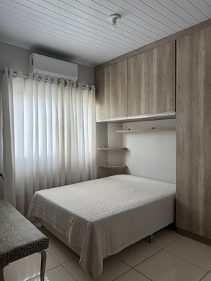 Ein Schlafzimmer mit einem Bett, einem kleinen Tisch, einem Kleiderschrank und einem Fenster mit Vorhängen.