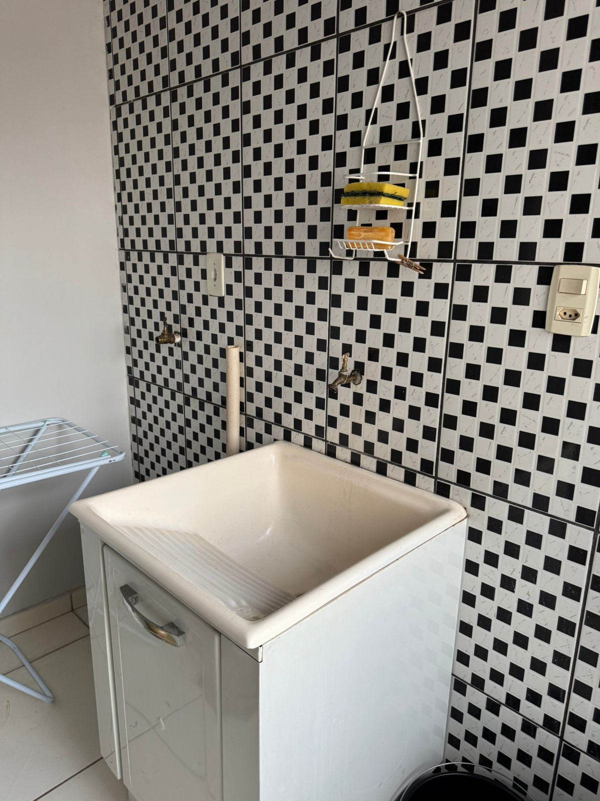 A small bathroom with a white sink, a checkered wall, and a metal drying rack.