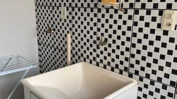A small bathroom with a white sink, a checkered wall, and a metal drying rack.